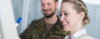 Frau und Soldat stehen vor Flipchart