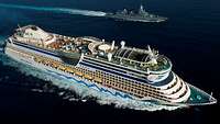Ein Kreuzfahrtschiff und ein Schiff der Marine fahren parallel auf hoher See