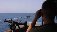 Ein Soldat beobachtet durch sein Fernglas ein Boot auf hoher See