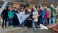 Menschen stehen als Gruppe vor der Kamera und halten eine dreieckige Flagge hoch.