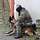 Ein Soldat und sein Schutzhund sitzen an einer Hausecke