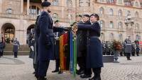 Soldaten stehen auf einen Platz und halten die Hände über eine Truppenfahne