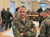 Ein Soldat mit deutscher Flagge auf der Schulter steht mit verschränkten Armen.