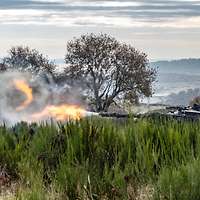 Ein Panzer im hohen Gras aus einem Hügel feuert auf ein Ziel in der Ferne.