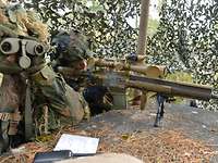 Zwei Soldaten unter einem Tarnnetz, einer mit Waffe, der andere mit einem Fernglas