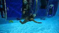Two soldiers get out of a training aircraft underwater.
