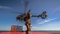 Ein bewaffneter Soldat auf einem Containerschiff. Im Hintergrund ein Hubschrauber.