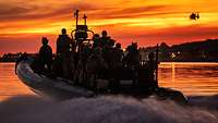 Mehrere Soldaten auf einem Schlauchboot vor einem roten Himmel.