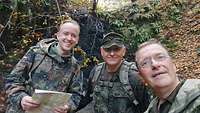 Zwei Soldaten und ein Militärgeistlicher blicken in die Kamera.