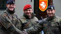Drei Soldaten haben jeweils eine Hand zur Mitte gelegt und schauen freundlich in die Kamera.