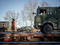 An einem Güterbahnhof steht ein Zug. Auf dem Waggon steht ein Soldat vor einem Lastwagen. 