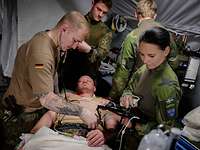 In einem Operationszelt wird ein Soldat operiert. Um ihn stehen vier Soldaten.