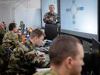In einem weißen Zelt sitzen Soldaten an Computern. Ein Soldat steht vor einer Leinwand.