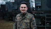 Ein Soldat steht in einem Feldlager vor militärischen LKW mit integrierten Arbeitskabinen.