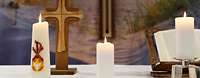 Drei brennende Kerzen, ein Holzkreuz und ein aufgeschlagenes Buch stehen auf einem Tisch
