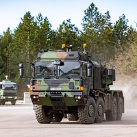 Ein LKW der Firma Rheinmetall steht neben einer Reihe anderer Lastkraftfahrzeuge, die unscharf zu erkennen sind.