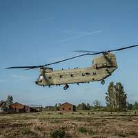 Ein Transporthubschrauber CH-47F Chinook der US Army landet auf einer Wiese, im Hintergrund zwei Häuser