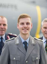 An elderly man and two soldiers stand together in front of an Airbus A400M