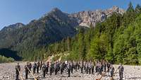 Das Gebirgsmusikkorps der Bundeswehr steht in einem ausgetrockneten Kiesbett dahinter die Alpen