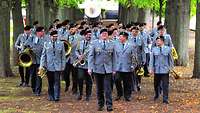 Musiker laufen mit Instrumenten in einer Allee und lachen miteinander