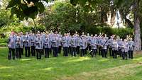 Musiker stehen mit Instrumenten auf einer Wiese zwischen Bäumen.