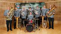 Musiker stehen mit ihren Instrumenten vor einer Leinwand und lächeln in die Kamera