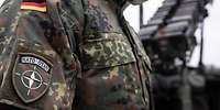Ein Soldat mit einem NATO-Ärmelabzeichen steht vor dem Waffensystem Patriot 