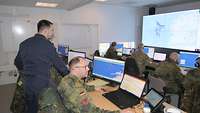 Soldaten in Uniform sitzen hinter Bildschirmen in einem Raum.
