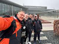 Vier Sportler posieren für ein Selfie vor einem Flughafengebäude mit der Aufschrift „Hannover Airport“