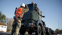 Ein Soldat steht vor einem Fahrzeug, das auf einen Zug verladen wird.