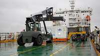 An Deck eines Schiffes verladen zwei Fahrzeuge einen Container