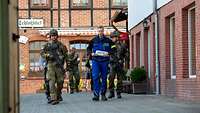 Ein Mann geht eine Straße entlang, begleitet von drei bewaffneten Soldaten.