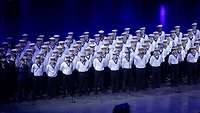 Mehrere Personen stehen in mehreren Reihen, in Marineuniform auf einer Bühne.