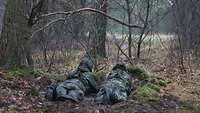 Zwei Soldaten liegen im Wald in einer gebauten Stellung und beobachten das Vorfeld.