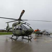 Drei Hubschrauber stehen auf einer großen Betonfläche. Der Boden ist nass.