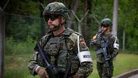 Militärische Wache Zwei bewaffnete Soldaten mit Armbinde „Wache“ laufen an einem Zaun entlang