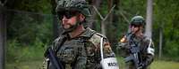 Zwei bewaffnete Soldaten mit Armbinde „Wache“ laufen an einem Zaun entlang