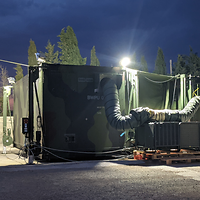 Auf einer Betonfläche stehen zwei Container im Tarnfleckmuster.