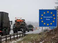 Militärische Fahrzeuge fahren hintereinander auf der Autobahn an einem polnischen Grenzübergangsschild vorbei.