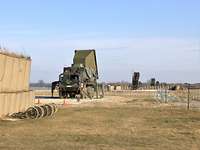 Ein militärischer LKW mit einer großen Radarplatte steht vor Raketenstartgeräten im Hintergrund.