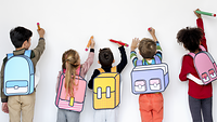 Fünf Kinder, die mit dem Rücken zur Kamera stehen. Sie malen mit großen Stiften an eine weiße Wand.