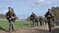 Eine größere Gruppe von Soldaten marschiert in zwei Reihen über einen Feldweg.