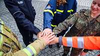 Menschen in unterschiedlichen Uniformen legen im Kreis ihre Hände übereinander