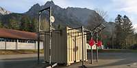 Ein Container mit Hanteln und Klimmzugstangen, im Hintergrund sind ein Gebäude und Berge.
