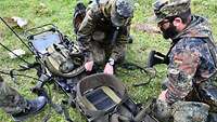 Zwei Soldaten hocken mit einer auseinandergeklappten Trage am Boden.