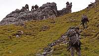 Soldaten mit Marschgepäck klettern einen steilen Berg hinauf, einige sind schon oben.