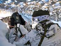 Ein Soldat fotografiert mit einer digitalen Kamera aus einem verschneiten Versteck heraus.