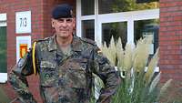 Ein Soldat mit goldener Kordel an der linken Schulter steht vor einem Gebäude.