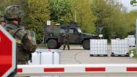 Hinter einer Schranke stehen Soldaten, ein Militärfahrzeug und weitere Hindernisse