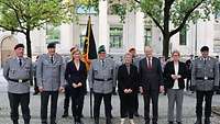 Soldaten und Zivilisten stehen nebeneinander. Hinter ihnen steht die Truppenfahne. 